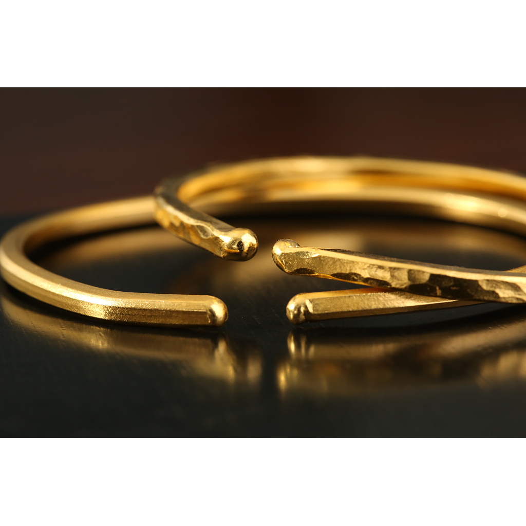 Close-up of handcrafted gold Viking-style cuff bracelets with smooth and hammered finishes, displayed on a dark surface for a rustic, elegant look